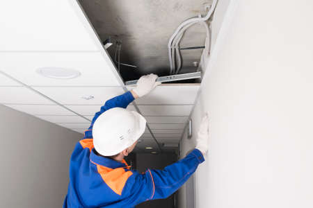 a worker in a helmet finishes the installation of a false ceiling, rear viewの写真素材