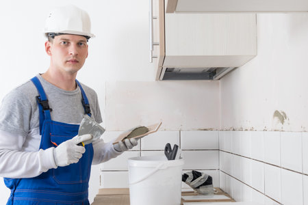 a worker in overalls applies glue to the tile with a spatula to lay itの写真素材