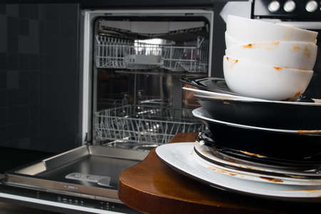 against the background of a built-in dishwasher, a stack of dirty plates and mugsの写真素材