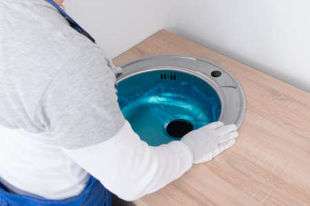 furniture assembler, inserted a metal sink into a cut-out hole in the countertop of the kitchen furnitureの写真素材