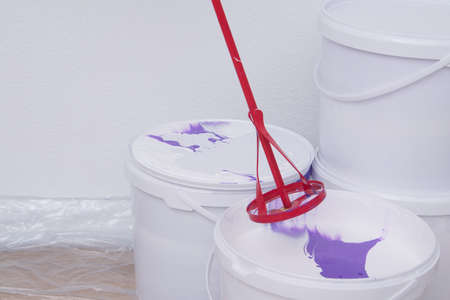 close-up of paint buckets and a stirrer, against a white wallの写真素材