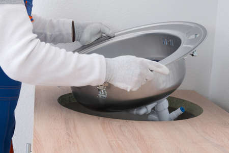 a specialist in protective gloves, installs a metal sink with an assembled white sewer pipe, in the opening of the countertop, close-upの写真素材