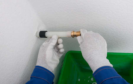 in a plastic pipe, a worker in protective gloves installs a copper adapter for plumbingの写真素材