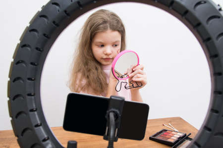 in the center of a circular lamp and a smartphone, a blogger girl makes a make-up, draws a heart on her cheekの写真素材
