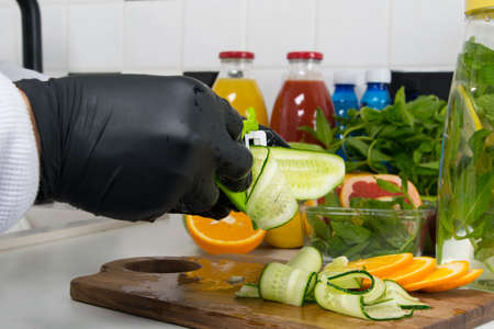 the chef's hands in black gloves, cut into thin slices of cucumber to add to a vitamin cocktailの写真素材