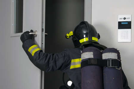 a firefighter in protective clothing and a hard hat, with fire extinguishing equipment, enters the doorway, rear viewの写真素材