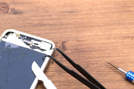 on a wooden table, a broken phone, lies to replace the case, next to tweezers, a screwdriver, a scalpel, there is a place for the inscriptionの写真素材