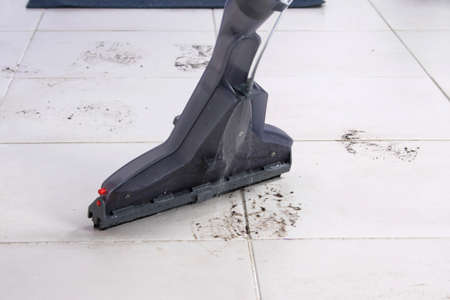 on the white tile, a washing vacuum cleaner removes dirty footprints from shoesの写真素材
