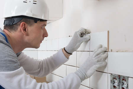 a construction worker in a protective helmet, applies a white tile to the wall, close-upの写真素材
