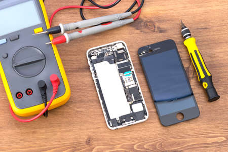 on a wooden table there is an electric tester equipment and a phone with a removed liquid crystal screen to replace itの写真素材