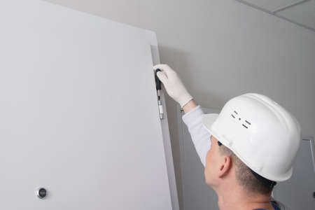 carpenter in uniform, adjusting the hinges of the front door, close-upの写真素材