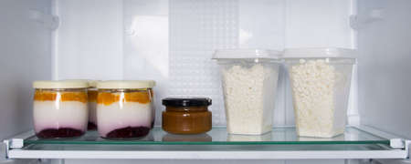 on the glass shelf of the refrigerator, there are cans of yogurt and fruit and grainy cottage cheese...