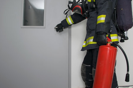 firefighter in protective clothing and with a fire extinguisher, opens the iron door, there is a place for the inscriptionの写真素材