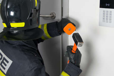 close-up of a firefighter in protective clothing and a hard hat trying to open a door with a sledgehammer and chiselの写真素材