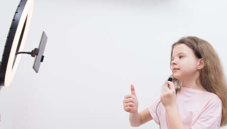 a girl blogger, in front of a circular light and a smartphone, checks the sound of the microphone and shows the classの写真素材