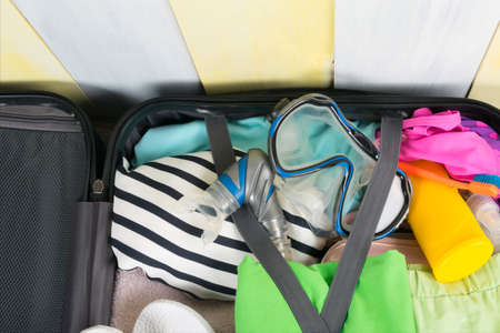 a set of things for travel and recreation, in an open suitcase, on a gray-yellow wooden backgroundの写真素材