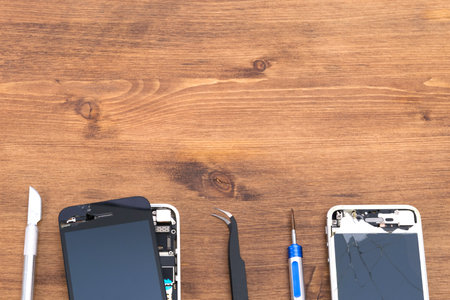 on a wooden table, a phone with a removed liquid crystal screen to replace it, a screwdriver and tweezers, there is a place for the inscriptionの写真素材