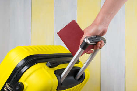 close-up of a hand holding a suitcase handle and passport documents, for travelの写真素材
