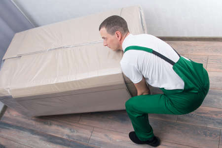 the loader is a man, picks up a large box of upholstered furniture, at the address of delivery to the apartmentの写真素材