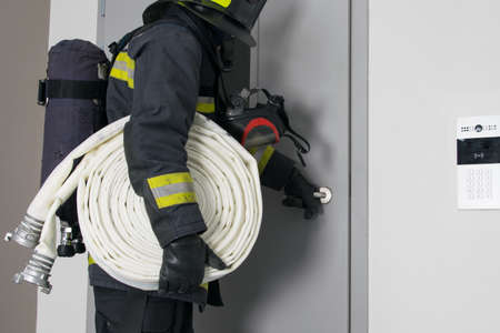 close-up, a firefighter in protective clothing, with fire fighting equipment, trying to open a closed door, on the wall of the video intercomの写真素材