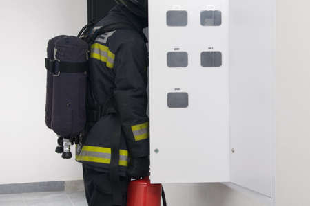 close-up of an electrical switchboard, a firefighter holding a fire extinguisher, checking for a fire, there is a place for an inscriptionの写真素材