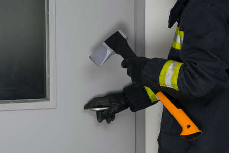 close-up of a firefighter in protective clothing in front of a metal closed door, breaking with an axの写真素材