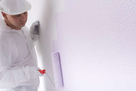 a painter in protective clothing, paints a white wall with a large roller, light purple color, there is a place for an inscriptionの写真素材