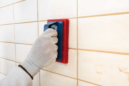 the hands of the master rubs the brown grout on white tiles with a special sponge, finishing work, close-upの写真素材