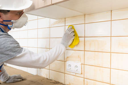 the master wipes the white ceramic tiles from the remnants of brown grout with a rag, finishing workの写真素材