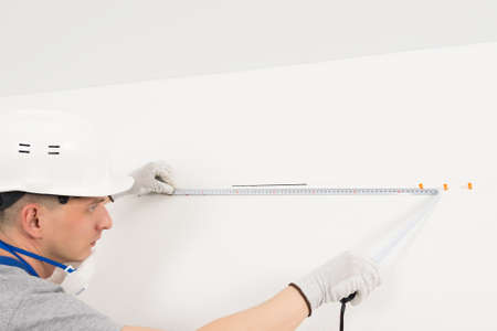 a worker measures the distance between the holes in the wall with a tape measureの写真素材