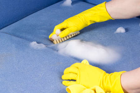 hand in a rubber glove dry cleaning upholstered furniture with a brush, close-up, side viewの写真素材