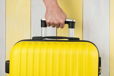 hand holds the handle of a yellow suitcase, close-upの写真素材