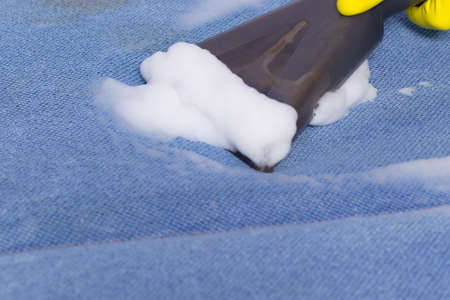 close-up cleaning a blue upholstered sofa with special foam using a brush on a vacuum cleanerの写真素材