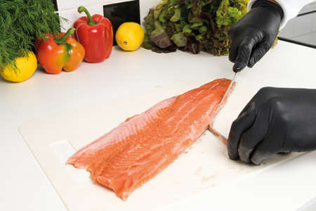 the chef's hands in gloves cut the fillet of red fish on the tableの写真素材