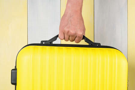 hand carries a suitcase on a yellow gray background, close-up, travel conceptの写真素材