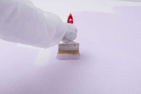 close-up of a builder's hand painting a white wall with a brush, in a light purple colorの写真素材