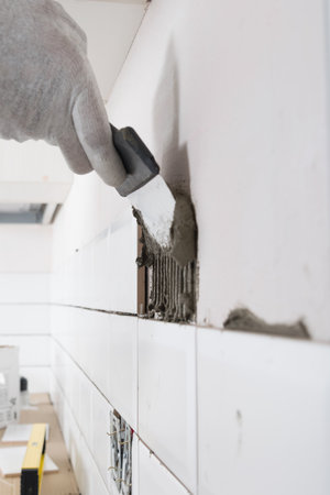 the process of applying white tiles to the wall, an iron spatula is applied to the solution, close-upの写真素材