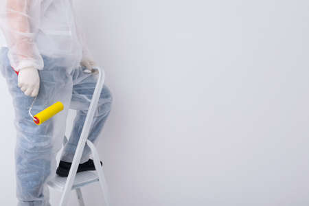 a construction worker in protective clothing is going to smooth the wallpaper on the white wall with a special roller, there is a place for the inscriptionの写真素材