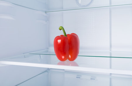 against the background of a white refrigerator, there is a red Bulgarian sweet pepper on a glass shelf, close-upの写真素材