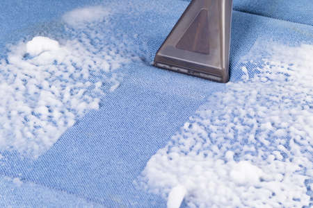 cleaning a dirty blue soft sofa with special foam using a brush on a vacuum cleanerの写真素材