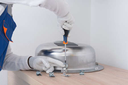 a specialist in protective clothing, installs mounting clips to fix the metal sink, twisting it with a screwdriverの写真素材