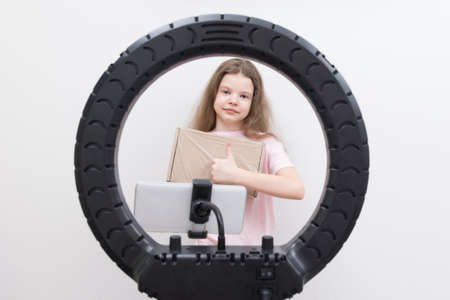 a girl blogger, in the center of a circular lamp and a smartphone, makes an overview of the package for unpacking and shows the classの写真素材