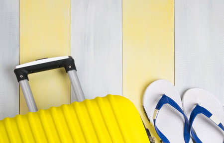 on a light background, a yellow travel suitcase and beach flip-flops, close-up, there is a place for the inscriptionの写真素材