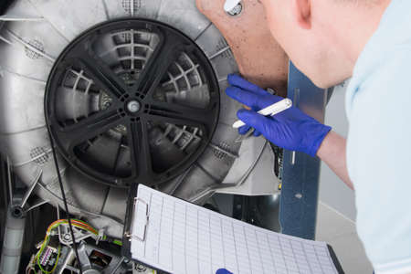 the master writes down the number of the fault in the breakdown of the washing machine, during the repair, clarification of the cost, close-upの写真素材