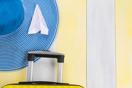 on the gray-yellow surface, a travel suitcase, a hat and a paper airplane, there is a place for the inscriptionの写真素材