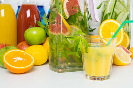 against the background of cut fresh citrus fruits and apples, a glass of juice from freshly squeezed oranges and a glass jug and bottles of lemonadeの写真素材