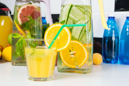 on a white table, a glass of freshly squeezed orange juice with a straw and jugs of refreshing lemonadeの写真素材