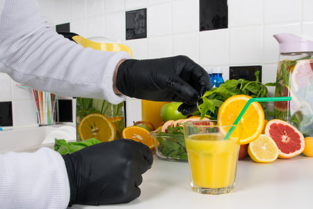 the chef's hands in black gloves decorate a glass of freshly squeezed orange juice, mint and fruitの写真素材