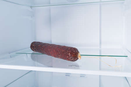 a loaf of sausage, in the refrigerator on a glass shelf, on a white background, close-upの写真素材