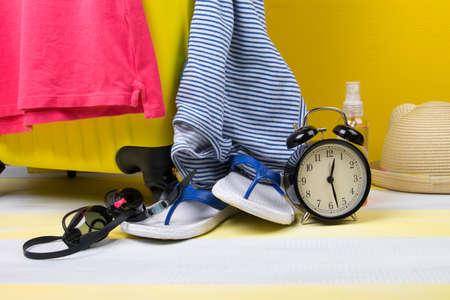 on a gray-yellow background, a set for travel and recreation, a suitcase, flip-flops, a hat, glasses and an alarm clockの写真素材